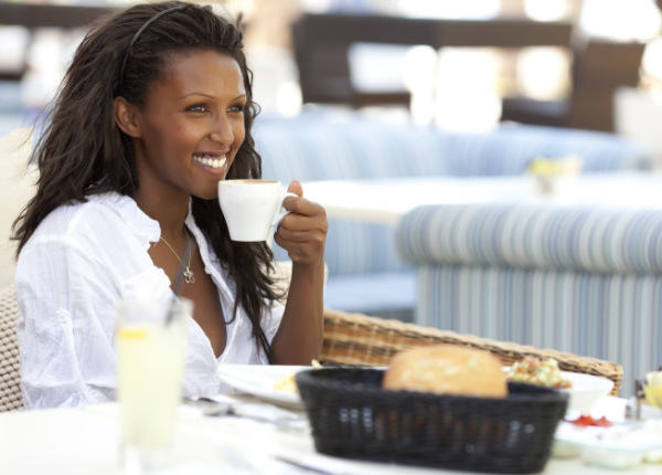 Good start breakfast Happy woman eating breakfast, holding cup of coffee in left hand.