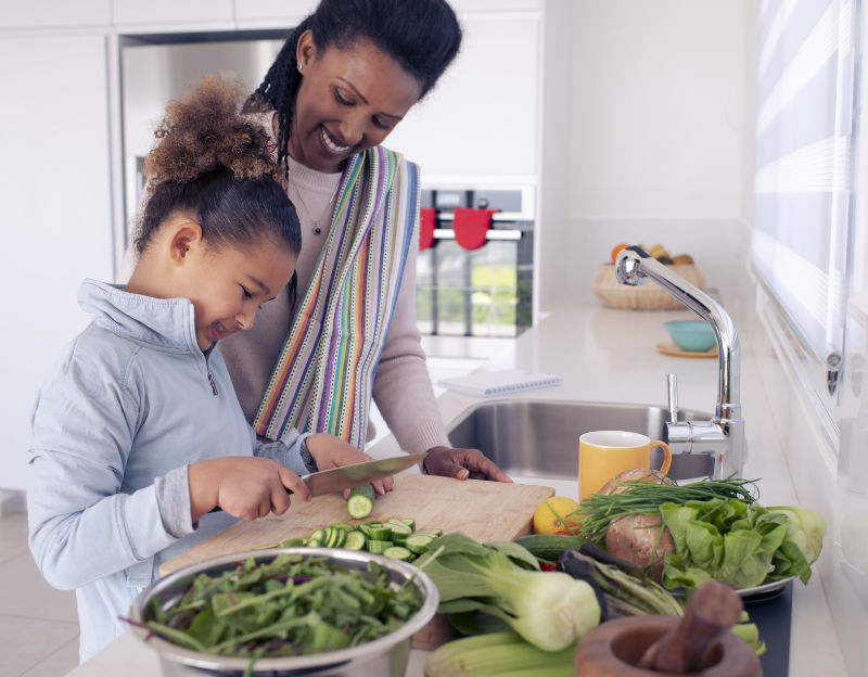 Pretty little girl assisting her mum, cutting cucumber for green salad. Render of a kitchen in Kefita apartments, Addis Ababa